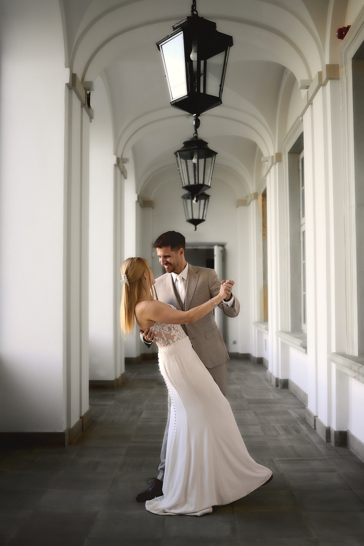 The newlyweds stand on a path in a formal garden among blooming magnolias.