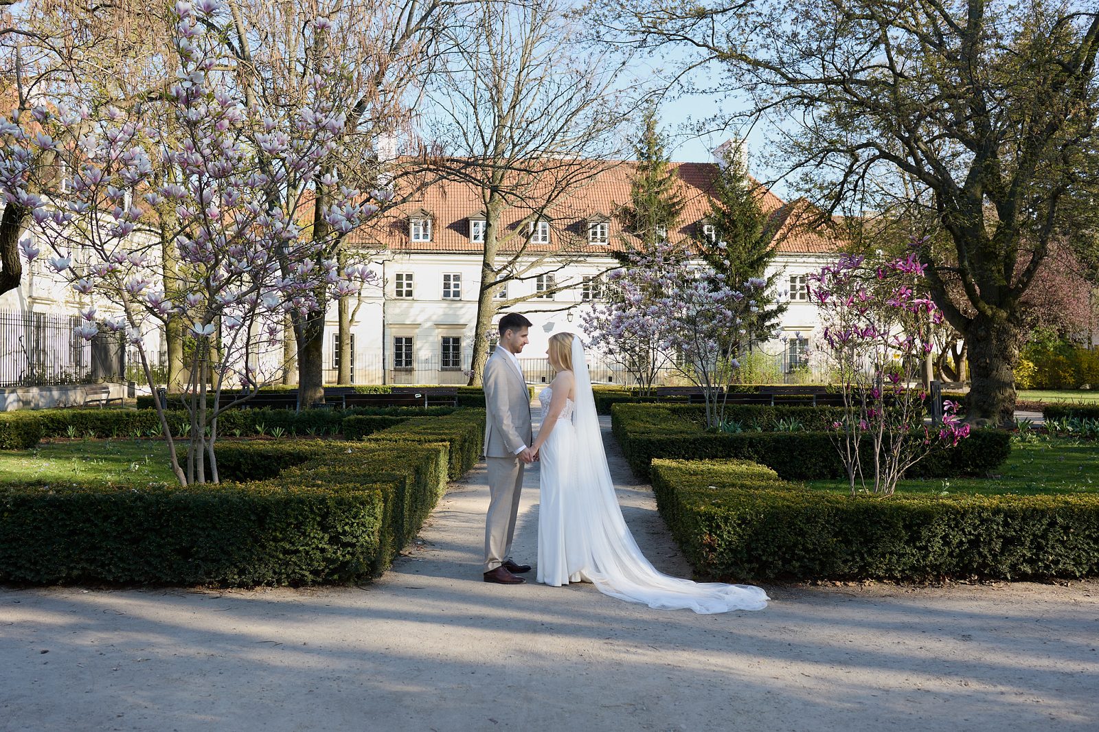 The newlyweds embrace in a garden of blooming magnolias, with a light-colored palace behind them.
