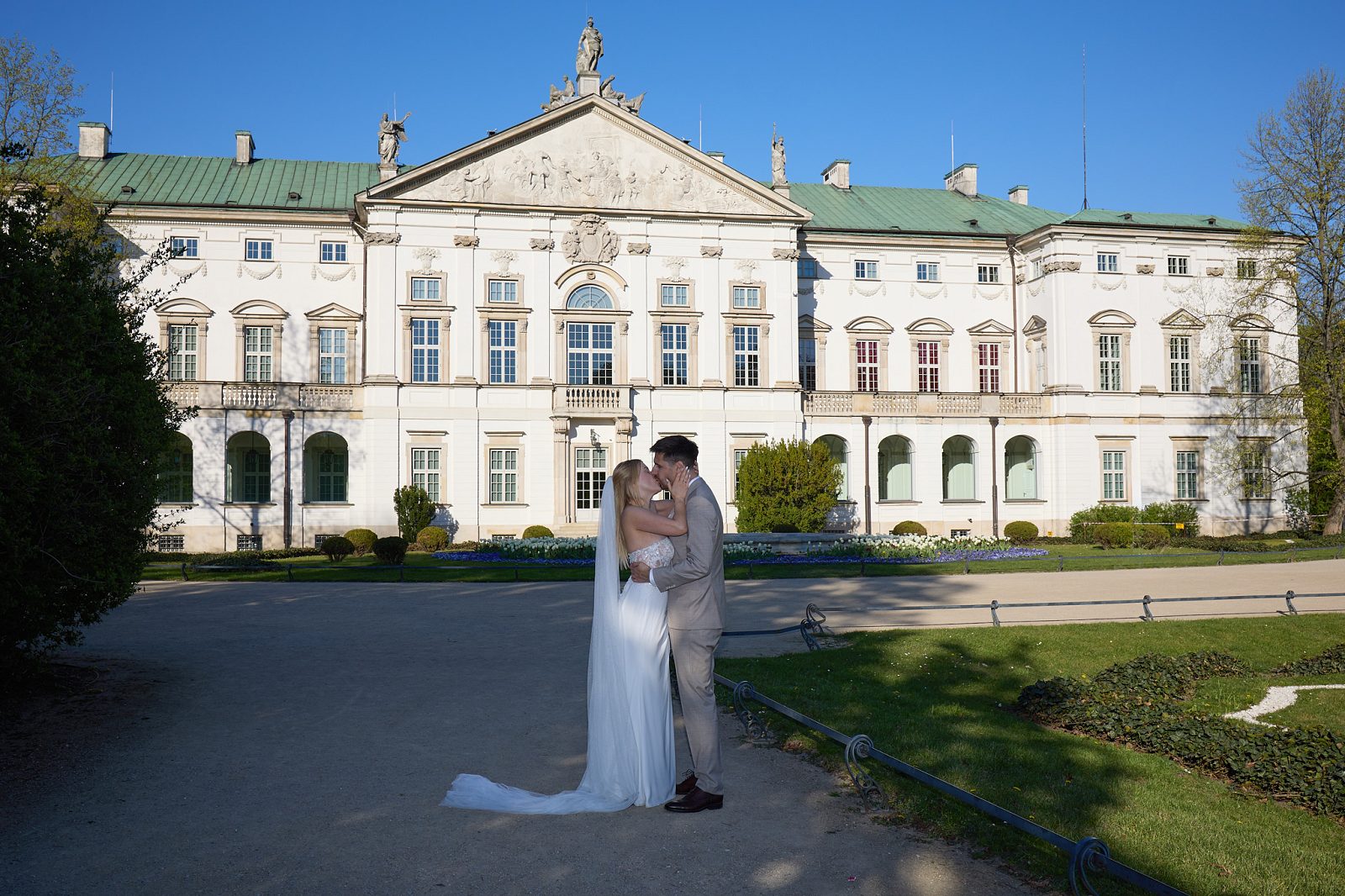 The newlyweds embrace in front of the palace’s neoclassical facade in a sunny garden.