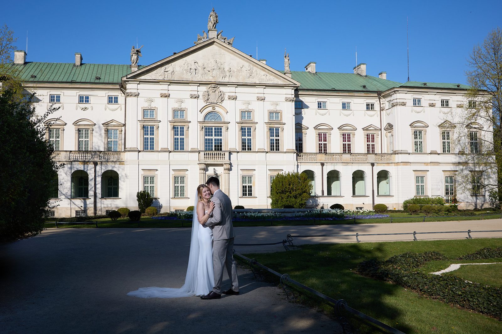 The newlyweds embrace in the palace garden in front of its facade.