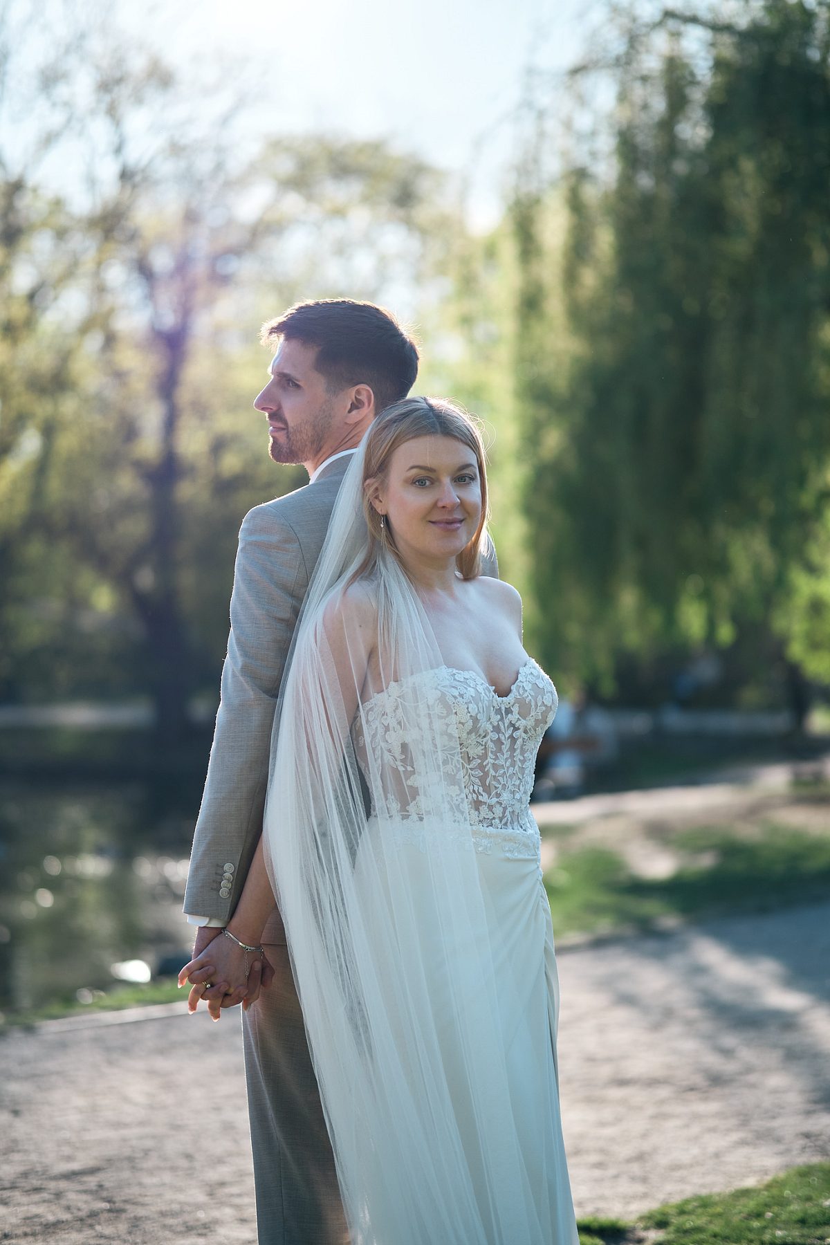 The bride stands in the foreground holding the groom’s hand on a garden path.