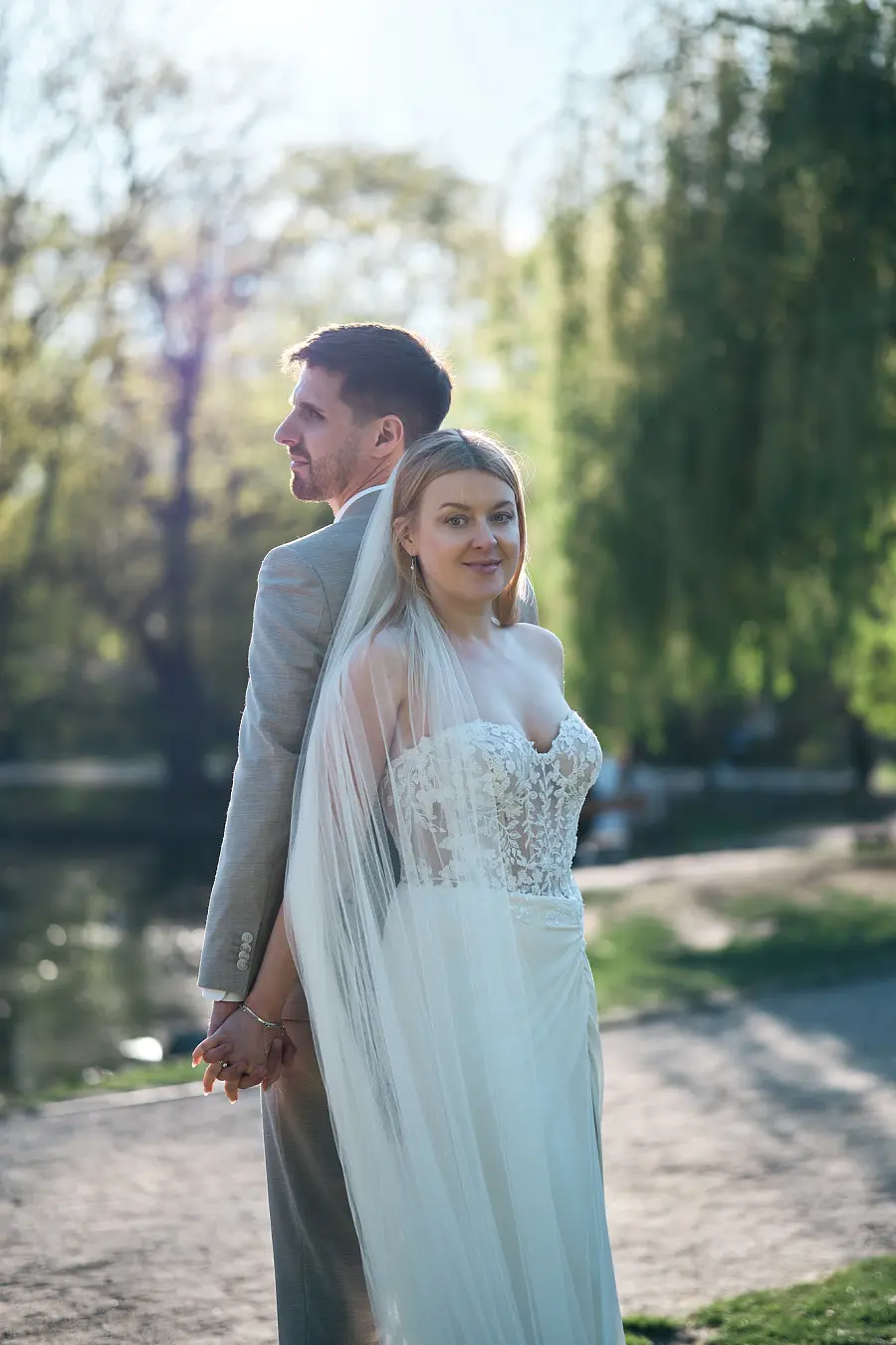 Невеста стоит впереди, держась за руку жениха на садовой дорожке.