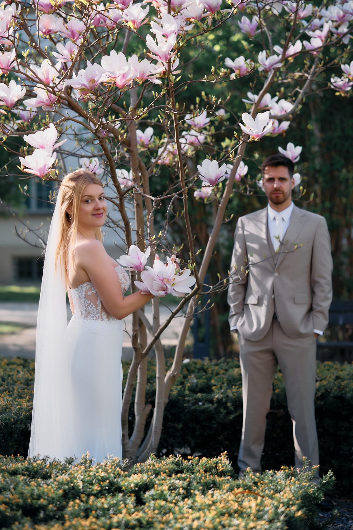 Portrait of the bride with a blooming magnolia branch in the foreground and the groom behind her.