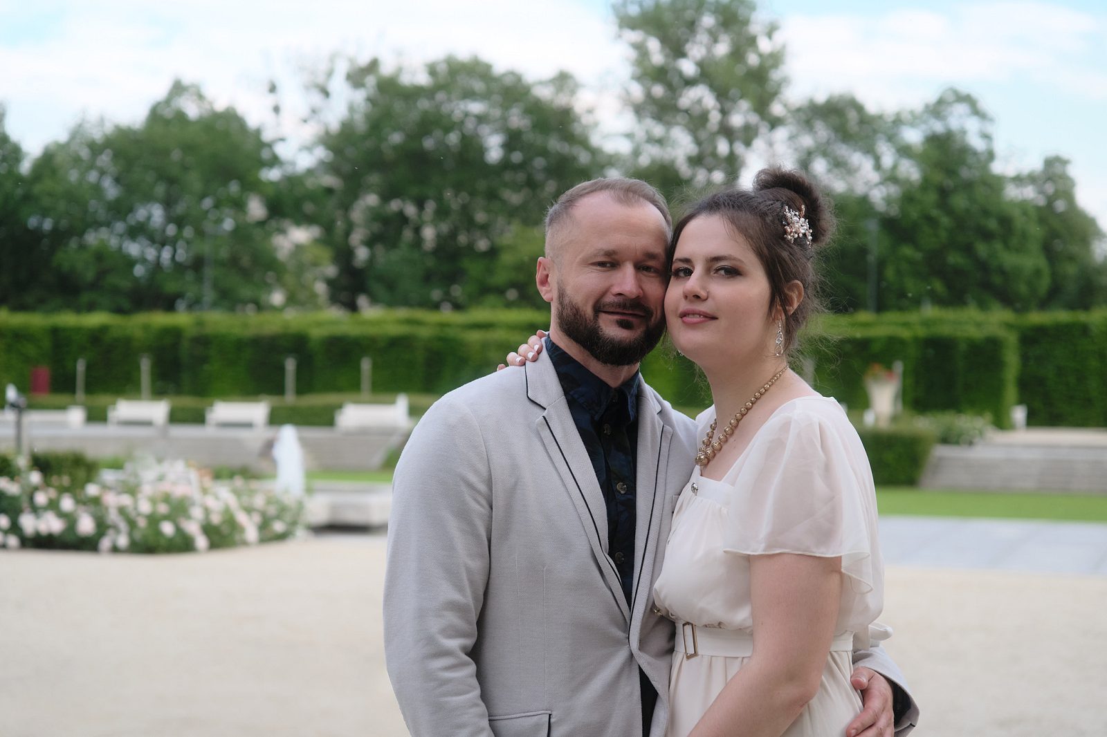 Жених обнимает невесту за талию в саду, а она кладёт руку ему на плечо.