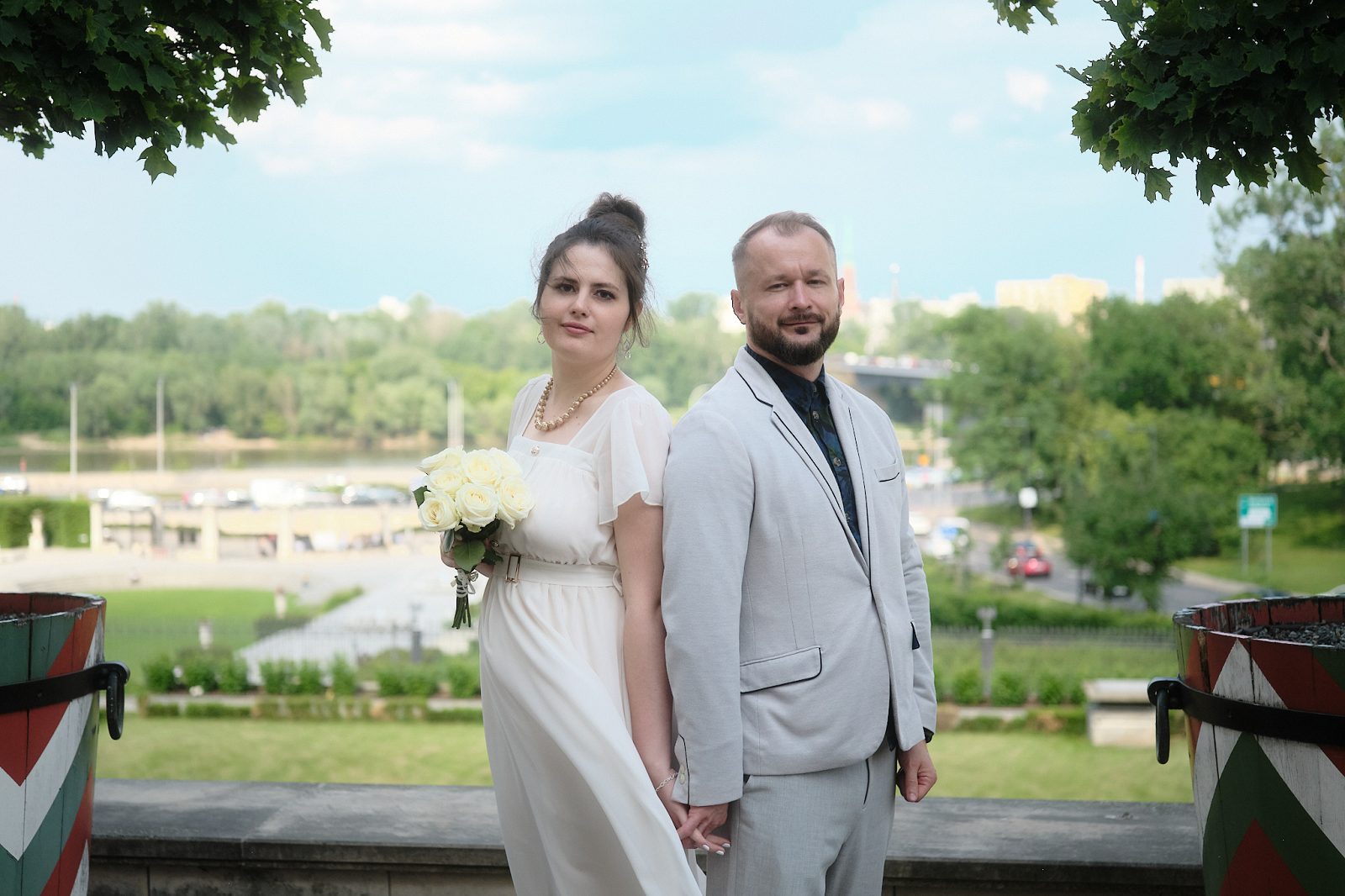 Жених и невеста целуются на террасе между деревьями, на фоне реки и города.