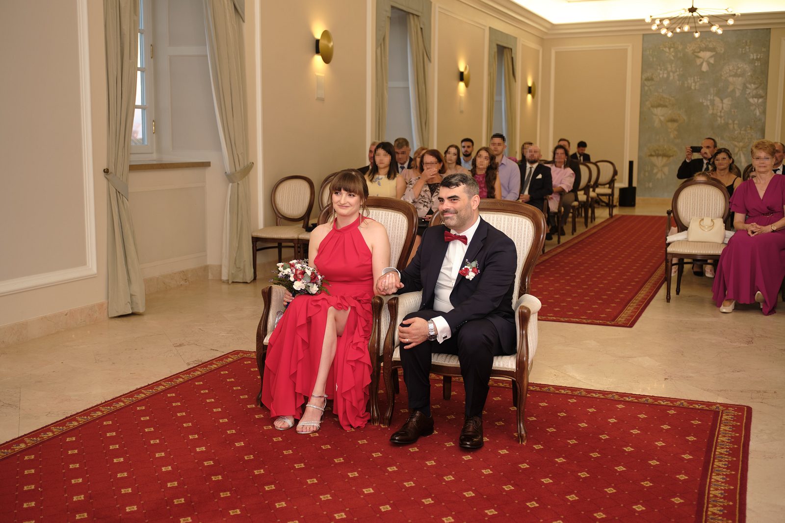 Para młoda siedzi w sali, a za nią widać gości.