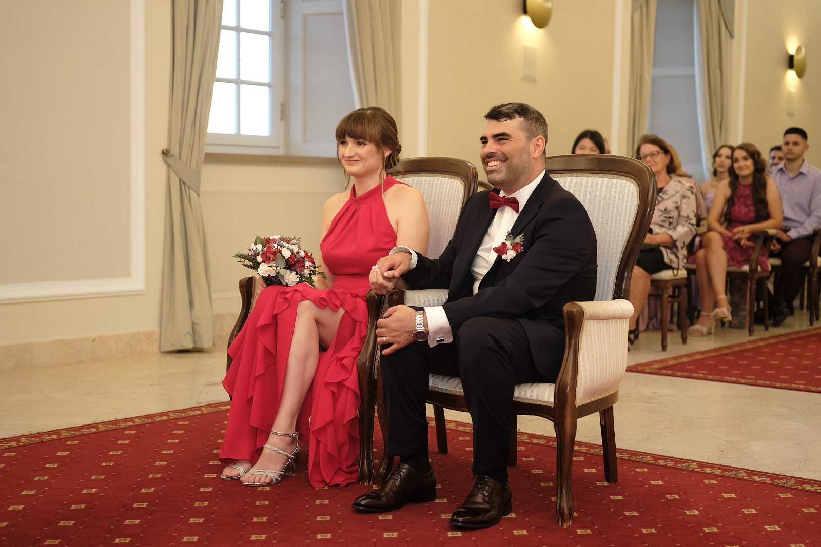 Panna młoda i pan młody siedzą obok siebie; przed nimi leży bukiet.