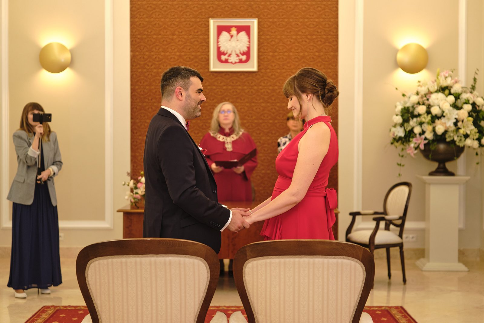Podczas ceremonii nowożeńcy łączą dłonie; po lewej widać urzędnika.