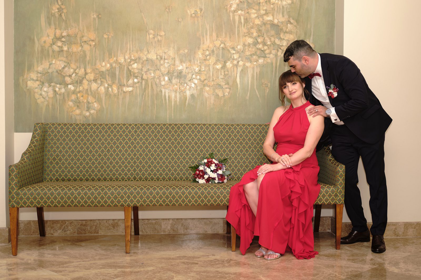 Pan młody całuje pannę młodą w czoło na kanapie.