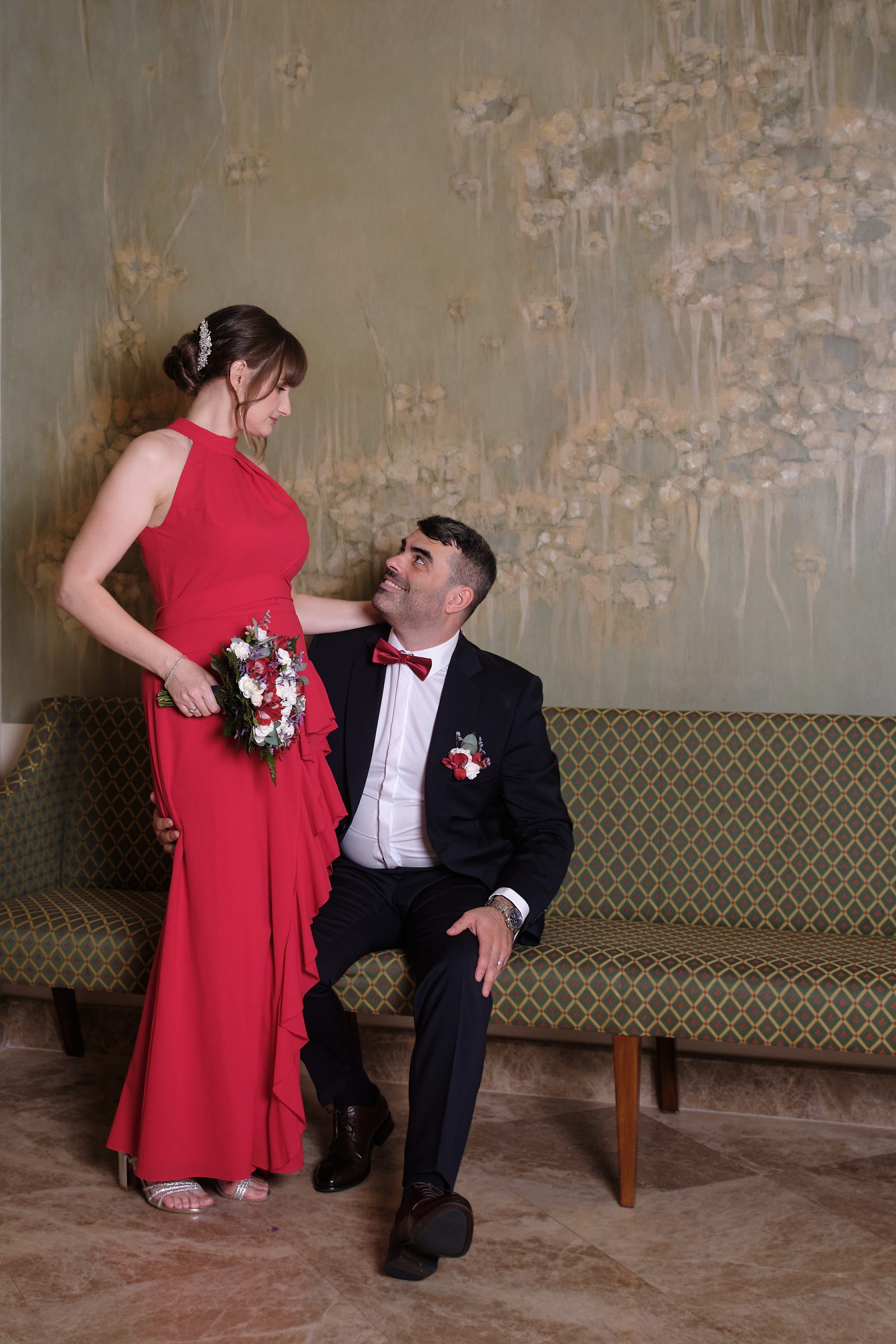 Panna młoda stoi przy kanapie obok siedzącego pana młodego; patrzą na siebie.