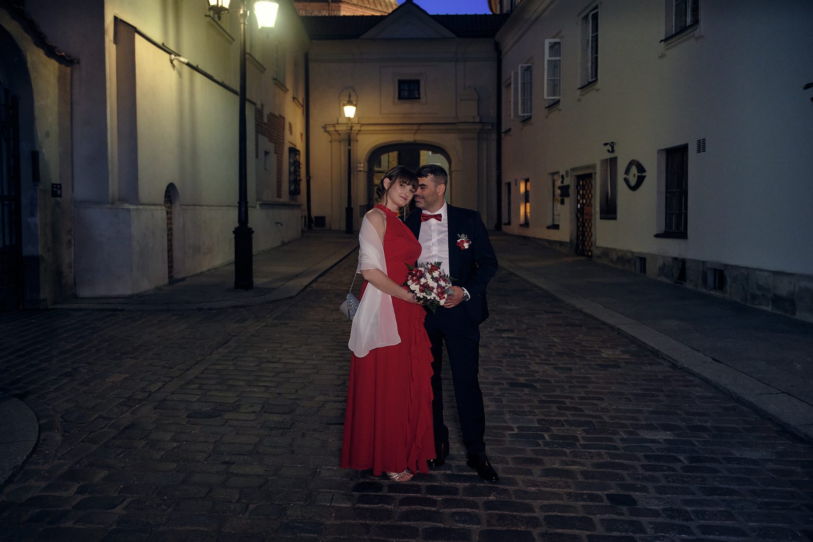 Nowożeńcy stoją razem nocą na brukowanej ulicy Starego Miasta.