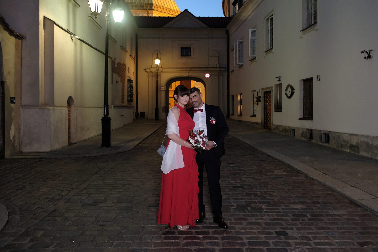 Portret nowożeńców na brukowanej ulicy w wieczornym świetle.